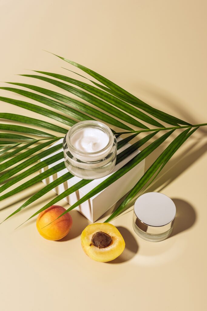 close up view of skin care products, apricots and green palm leaf on beige backdrop